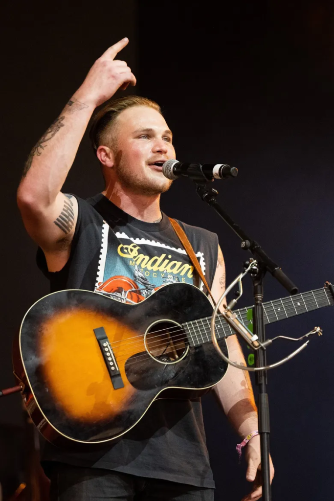 Zach Bryan performing live on stage while playing an acoustic guitar