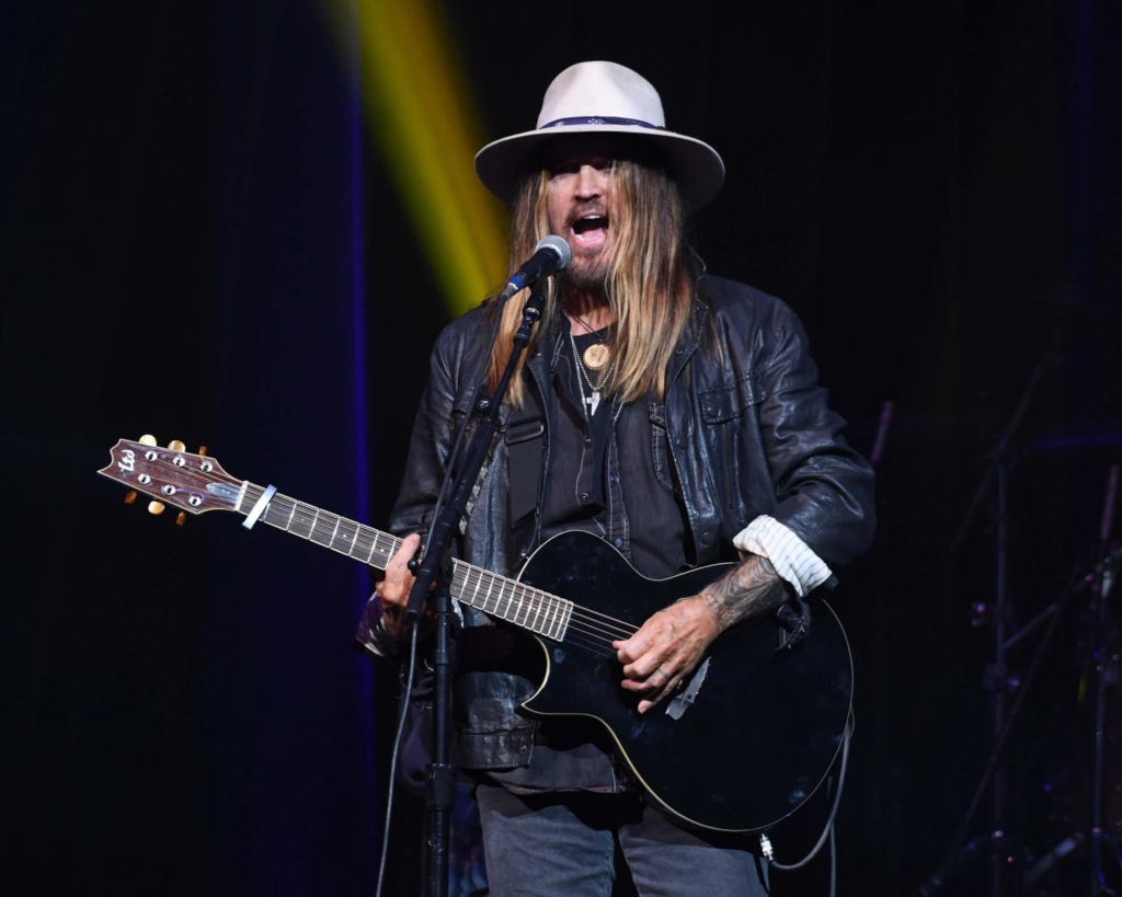 Billy Ray Cyrus performing live on stage while playing a black acoustic-electric guitar