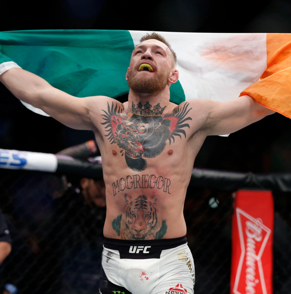 Conor McGregor celebrating a victory, specifically his historic win at UFC 205 where he became the first fighter in UFC history to hold titles in two weight classes simultaneously