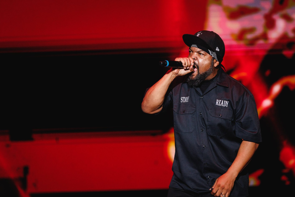 Ice Cube performing on stage in a black polo shirt