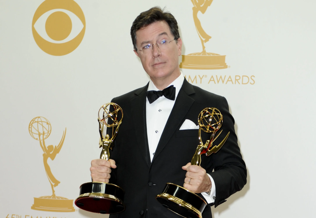 Stephen Colbert holding two Emmy awards in the press room after winning at the 65th Annual Primetime Emmy Awards in 2013