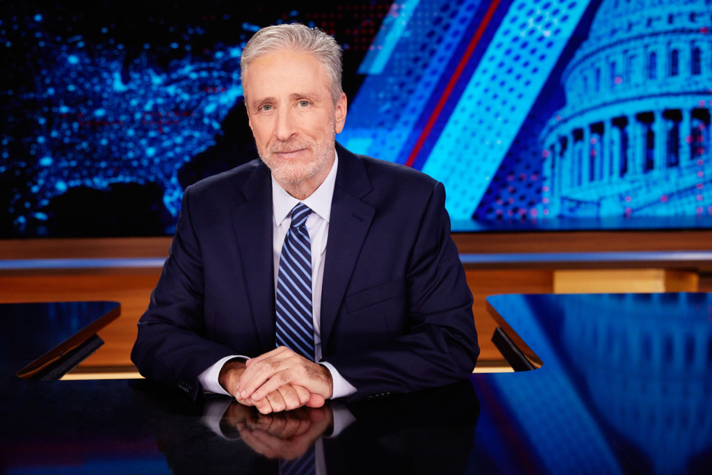 Jon Stewart behind The Daily Show news desk