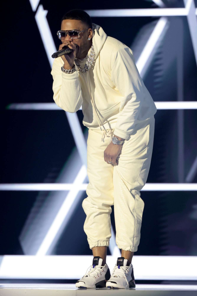 Nelly performs onstage wearing a cream-colored hoodie and matching jogger pants