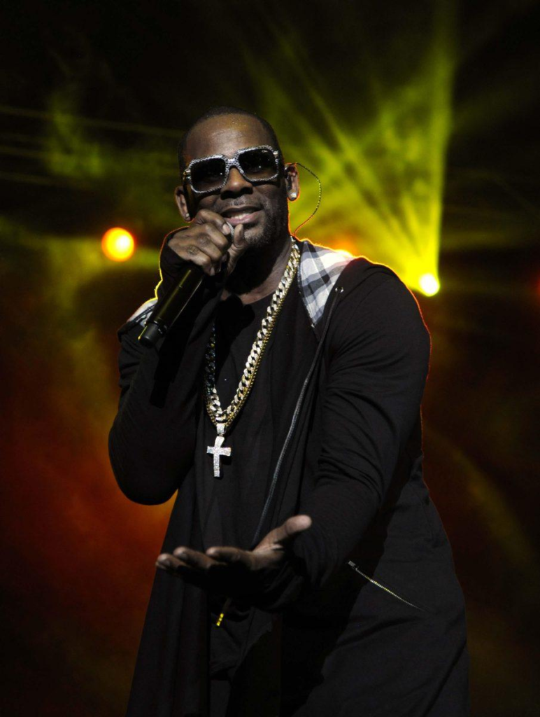 R. Kelly performing on stage wearing sunglasses and a large cross necklace