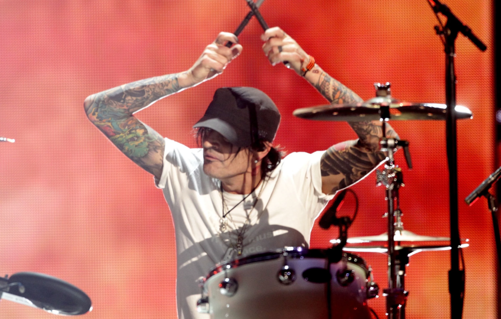 Tommy Lee performing on stage wearing a baseball cap