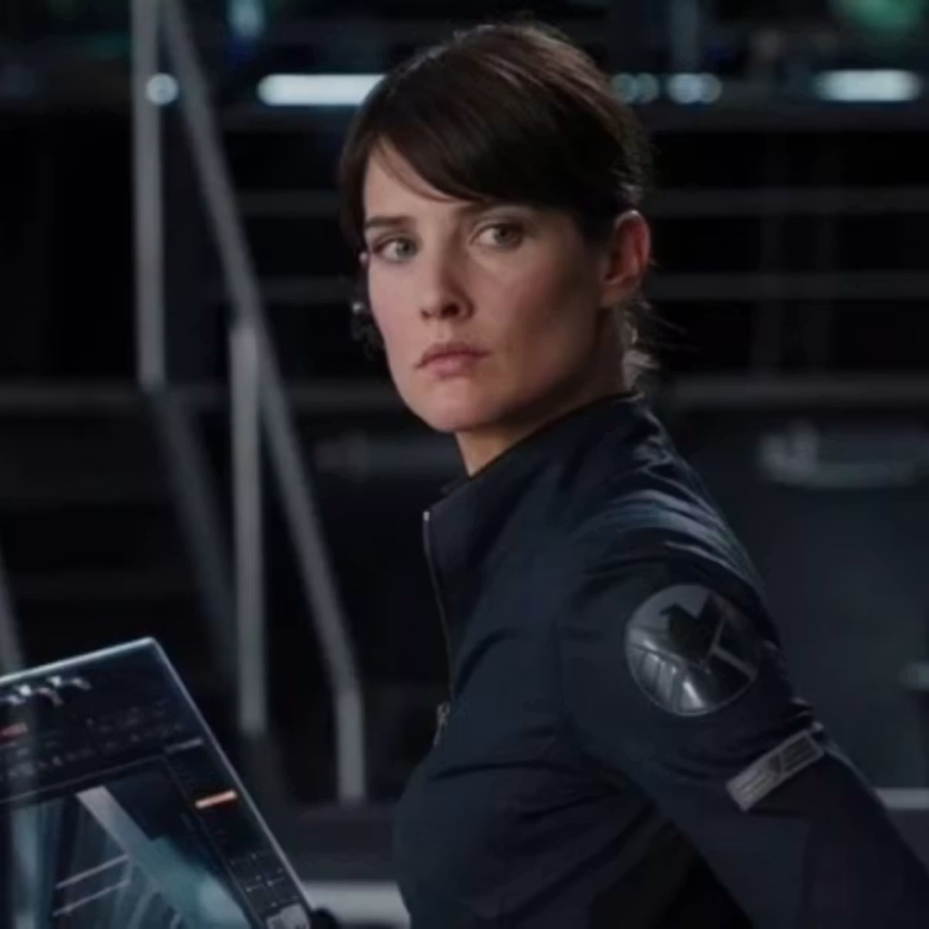 Cobie Smulders as Maria Hill wearing a black high-collar jacket with a S.H.I.E.L.D. insignia on the shoulder in the Marvel Cinematic Universe