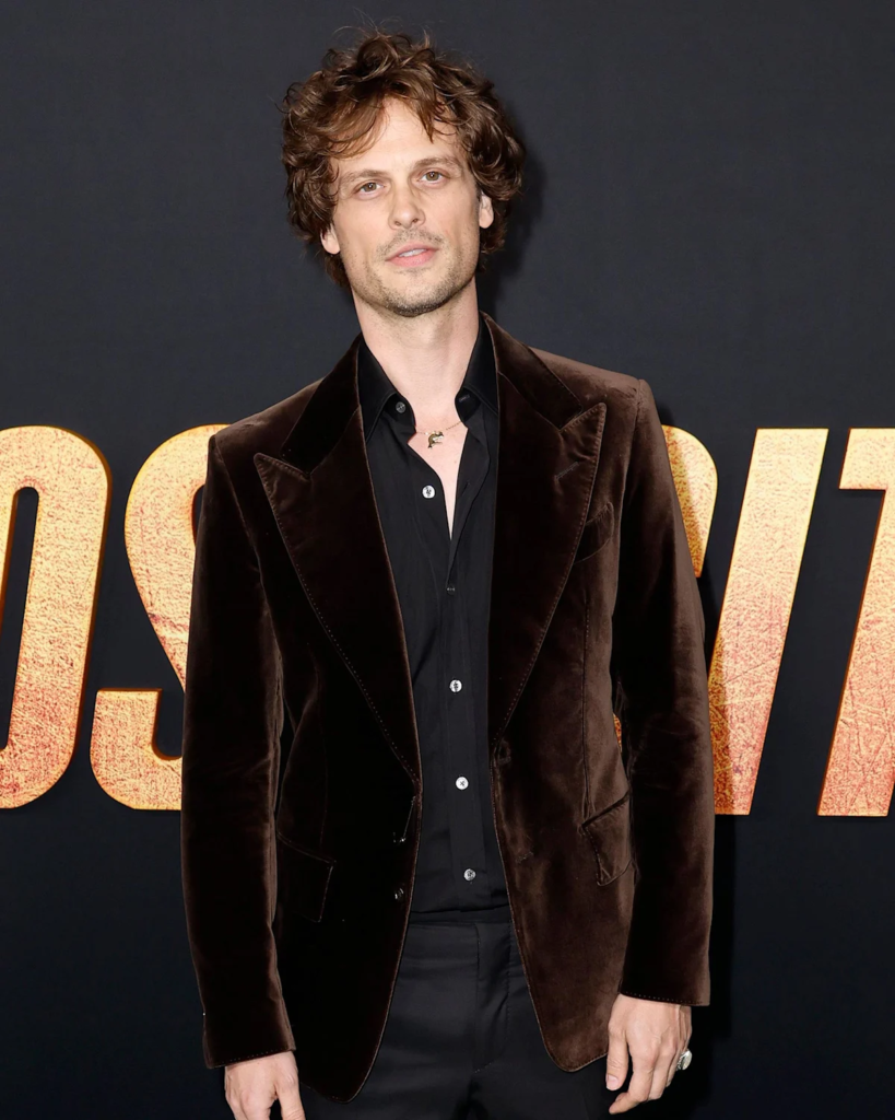 Matthew Gray Gubler is wearing a luxurious dark brown velvet blazer over a black button-down shirt