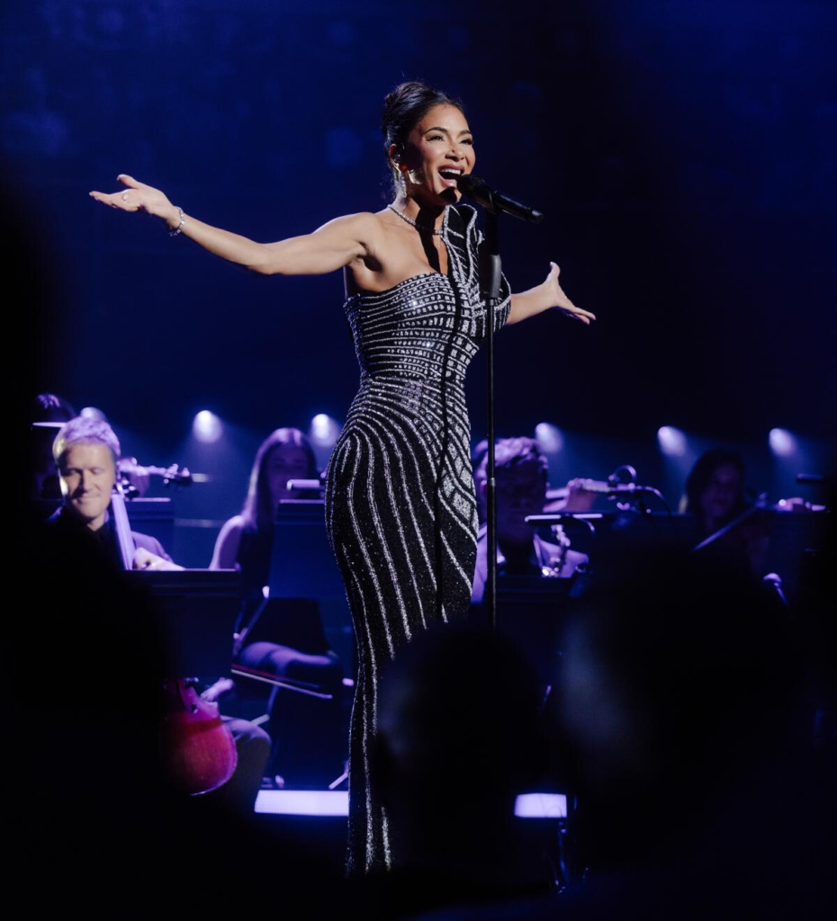 Nicole Scherzinger wears a dramatic one-shoulder evening gown covered in intricate, vertical beaded stripes while performing at London's Royal Albert Hall