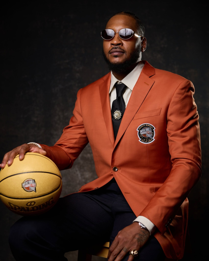 Carmelo Anthony wearing an orange Hall of Fame blazer at his official induction ceremony