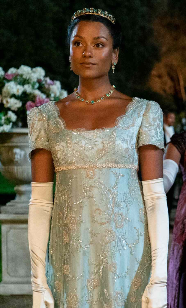 Simone Ashley as Kate Sharma in Bridgerton, wearing an intricate, light blue Regency-style gown with a low, scalloped neckline