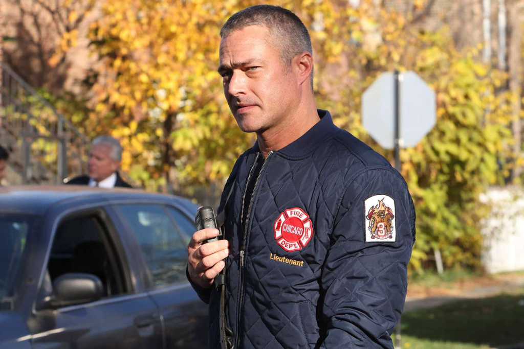 Taylor Kinney on the set of Chicago Fire, featuring a branded black bomber jacket with the Chicago Fire Department emblem