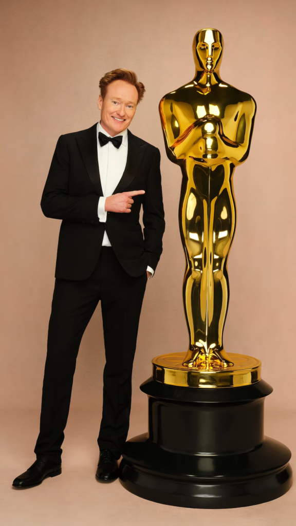 Conan O'Brien posing next to an oversized Oscar statuette in promotional imagery for the 97th Academy Awards