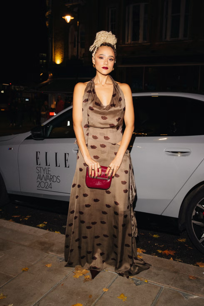 Nathalie Emmanuel wears a printed halterneck silk gown paired with a small red clutch bag on the red carpet at the ELLE Style Awards