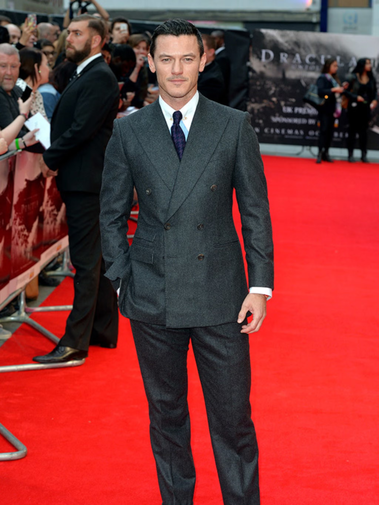 Luke Evans wears a sharp charcoal double-breasted suit with a crisp white shirt and dark tie while walking the red carpet at the premiere of Dracula Untold in London