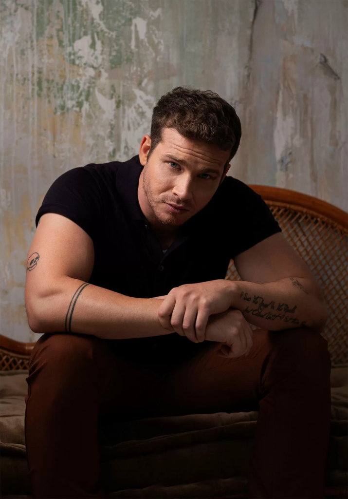 actor Oliver Stark wearing a black short-sleeved polo shirt
