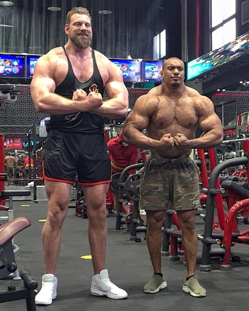 Dutch actor and bodybuilder Olivier Richters (left), known as "The Dutch Giant," standing alongside powerlifter and strength athlete Larry Wheels (right) in a gym